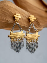 Gold and silver earrings trust model with chain details on a wooden stand.