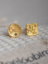 A pair of gold vermeil earrings with engraved text 'Oui' and 'A la vie' on a textured background.