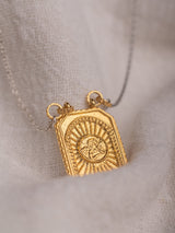 A gold vermeil Angelito necklace handmade by Leeloobird Jewelry Bali with a square-shaped medallion pendant, displayed on a textured fabric.