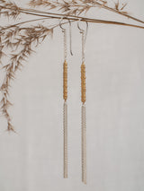 Sunny earrings by Leeloobird Jewelry brand in Bali featuring gold vermeil accents shaped like sun rays, attached to sterling silver 925 ear wires, displayed against a neutral background with dry plants to the side.