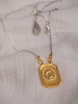 A gold vermeil Angelito necklace handmade by Leeloobird Jewelry Bali with a square-shaped medallion pendant, displayed on a textured fabric.