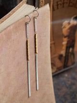 Sunny earrings by Leeloobird Jewelry brand in Bali featuring gold vermeil accents shaped like sun rays, attached to sterling silver 925 ear wires, displayed against a neutral background with dry plants to the side.