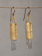 Presence earrings by LeeLoobird Jewelry brand in Bali featuring a geometric design with a shiny gold upper section and a textured silver lower section, suspended from gold hooks.